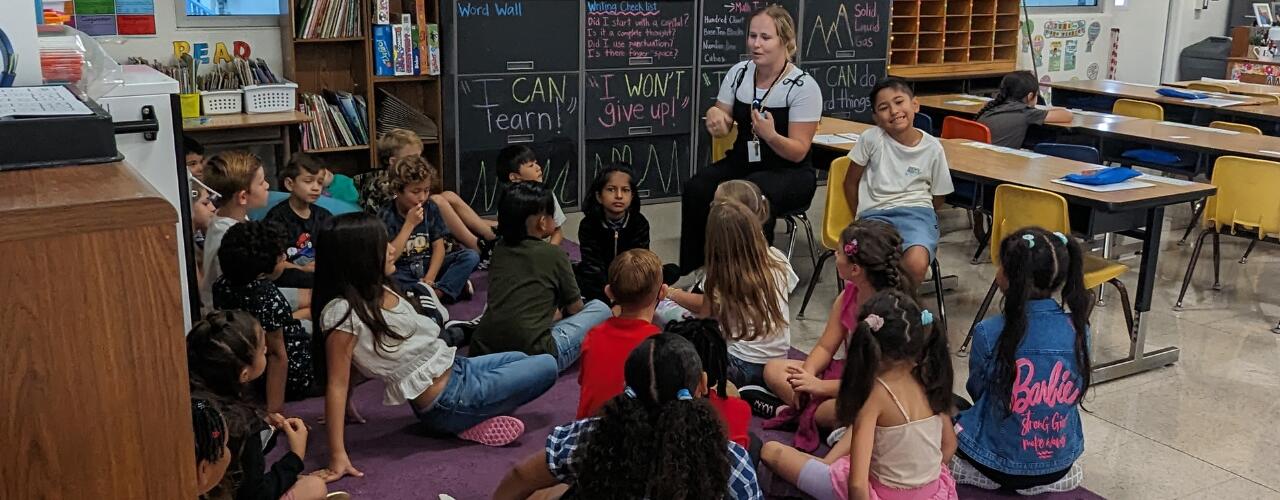 Photo of a teacher talking to her students who are sitting on the rug in the classroom