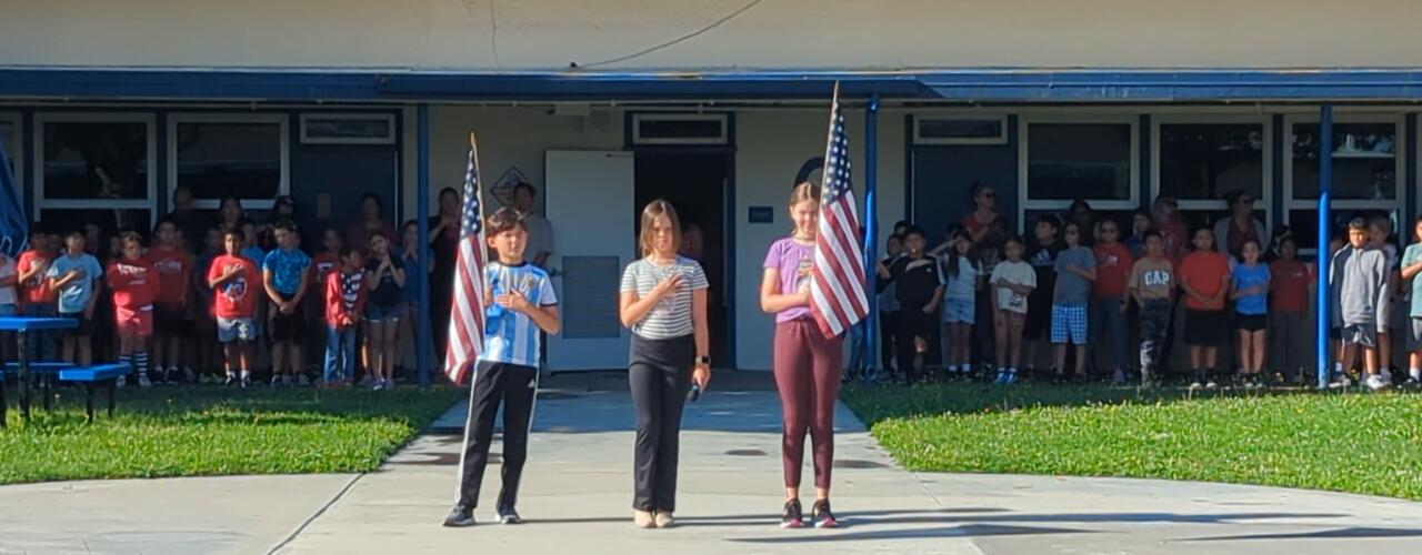 Photo of 3 students holding American flags and leading the pledge during the flag assembly